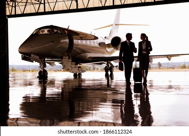 Silhouette of Businessman and Businesswoman walking away from the private jet in hangar