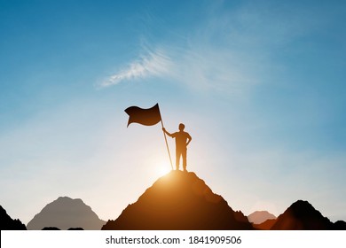 Silhouette of businessman holding flag on the top of mountain with over blue sky and sunlight. It is symbol of leadership successful achievement with goal and objective target. - Shutterstock ID 1841909506
