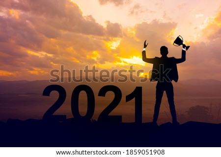 Silhouette businessman holding up a gold trophy cup as a winner in a competition and  2021 years with sunset background,Success new year concept.