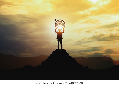 Silhouette of businessman holding a target board on top of mountain. Concept of aim and objective achievement.