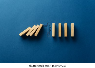 Silhouette of businessman on navy blue background stopping falling dominos in a conceptual image. With copy space.