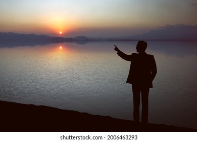 Silhouette of businessman pointing something on the lake with sunset sky background - Shutterstock ID 2006463293