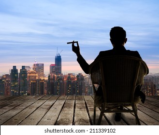 Silhouette of businessman sit on chair and hold a cigar and looking at the city in night. - Shutterstock ID 211339102