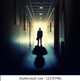 Silhouette of businessman standing in office building corridor against light