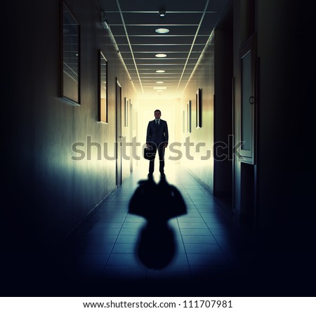 Silhouette of businessman standing in office building corridor against light