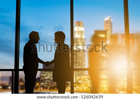 Silhouette businessmen shake hands finishing a deal between businesses Success of the joint venture business growth progress and potential concept over blurred employees the city night and flare light