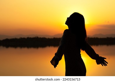 SILHOUETTE: Calm beautiful smiling young asian woman in white dress breathing fresh air outdoor on peaceful evening. relaxing with eyes closed, feeling alive, breathing, dreaming.