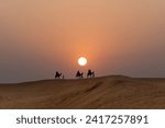 Silhouette of camels in the desert with people at sunset