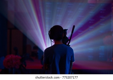 Silhouette Of A Cameraman Handling A Live Feed Camera With Ray Of Light In The Background.