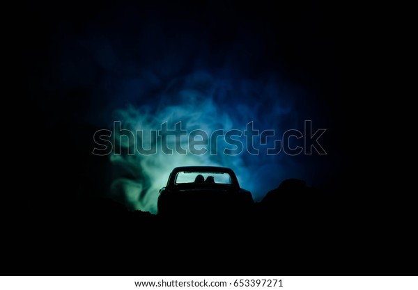silhouette of car with couple inside on\
dark background with lights and smoke. Romantic\
scene