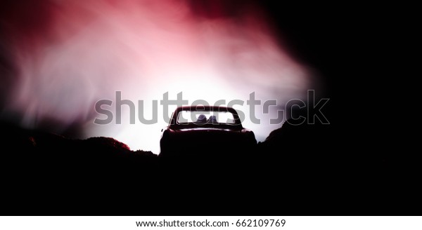silhouette of car with couple inside on\
dark background with lights and smoke. Romantic\
scene