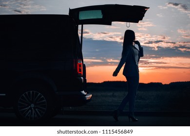 Silhouette Of Car And Girl At Sunset. Girl Near Van Open Trunk 