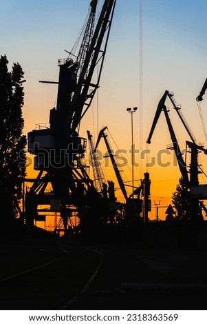 Silhouette of of cargo cranes. Port wharf landscape. Bright sunset, bright sky. Evening in port, sea, river dock