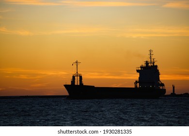 A Silhouette Of A Cargo Ship At Sunset.