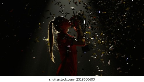 Silhouette of Caucasian woman female soccer football player raising a trophy above head against bright light and falling confetti. Super slow motion, shot on RED cinema camera - Powered by Shutterstock