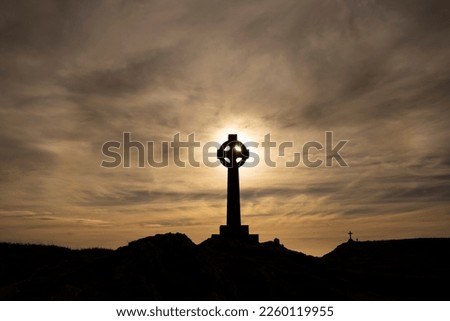 Silhouette of a Celtic cross with the evening sun directly behind it.  With a Christian cross in the background