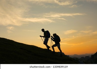 SILHOUETTE: Cheerful tourist couple are trekking up a grassy hill at breathtaking golden sunset. Young woman and boyfriend on active summer vacation hiking and exploring the breathtaking Julian Alps.
