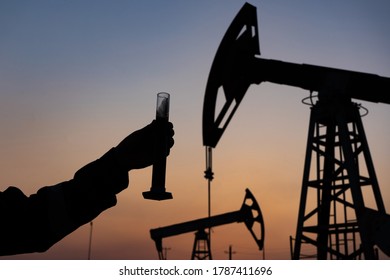 Silhouette Of A Chemical Engineer Taking A Sample Of Crude Oil Against The Background Of Oil Pumps.