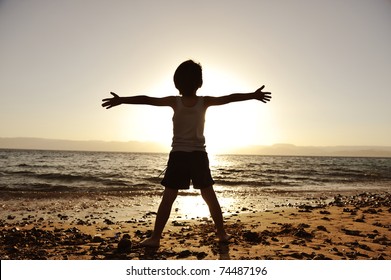 Silhouette of child on the beach, holding his hands up, hugging the sun - Powered by Shutterstock