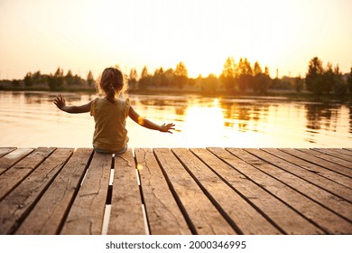 Silhouette of a child sitting on the wooden pier and enjoying heat summer evening at the lake at sunset. Heat summer, summer evenings in nature, spending time in the fresh air - Powered by Shutterstock