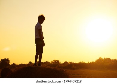 Silhouette of a child-boy standing on a haystack against the background of a field with a beautiful sunset.The concept of a carefree childhood. Beautiful summer landscape, copyspace. - Powered by Shutterstock