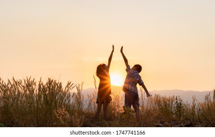 Silhouette der Kinder, die bei Sonnenuntergang mit erhobenen Händen auf dem Berg spielen.