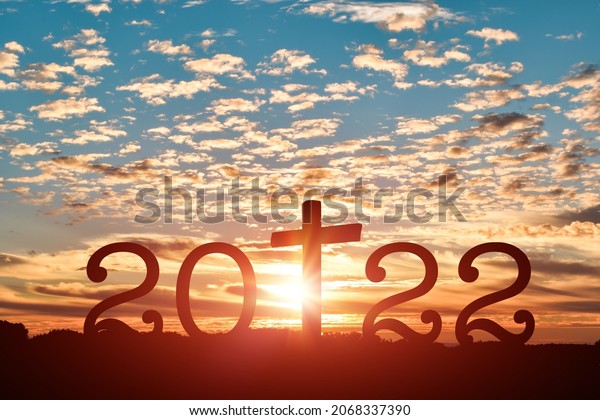 Silhouette of Christian cross
with 2022 years at sunset background. Concept of Christians new
year 2022
