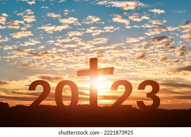Silhouette of Christian cross with 2023 years at sunset background. Concept of Christians new year 2023