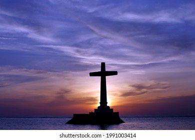 A silhouette of Christian cross on the stone thumb in the lake against a bluish sunset sky