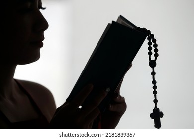 Silhouette Of A Christian Woman Reading The Bible With Prayer Beads.  Vietnam.  08-30-2018