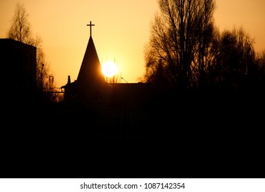 Silhouette of a church against the backdrop of the setting sun in a town.