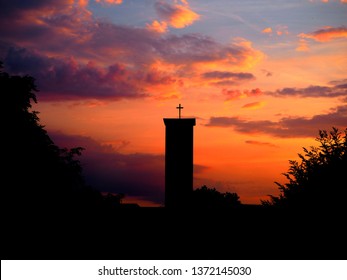 Silhouette of church with cross with spectacular sunset and orange sky in the background. Photo shot at Bindermichl in Linz, Austria.