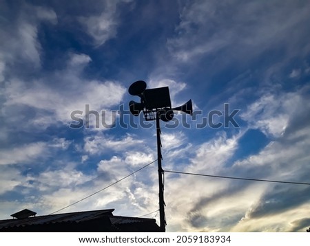 A silhouette of a civil defense siren in the background of the cloudy sky