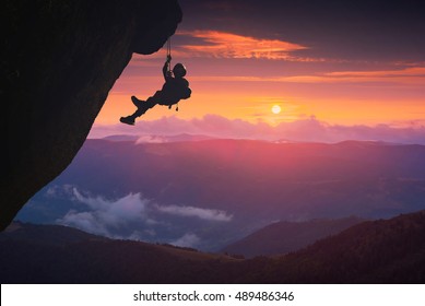 Silhouette of climber on a cliff against sunset in a mountain valley.