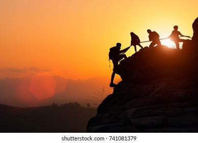 Silhouette of the climbing team helping each other while climbing up in a sunset. The concept of aid. 