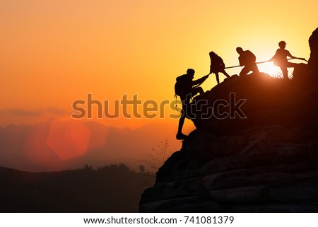 Silhouette of the climbing team helping each other while climbing up in a sunset. The concept of aid. 