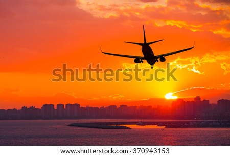 silhouette of commercial plane flying over a city during sunrise