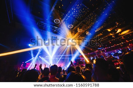 silhouette of concert crowd in front of bright stage lights. Dark background, smoke, concert  spotlights, disco ball