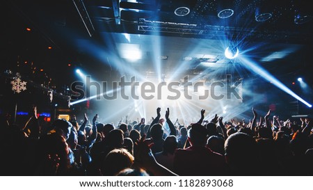 silhouette of concert crowd in front of bright stage lights. Dark background, smoke, concert  spotlights, disco ball