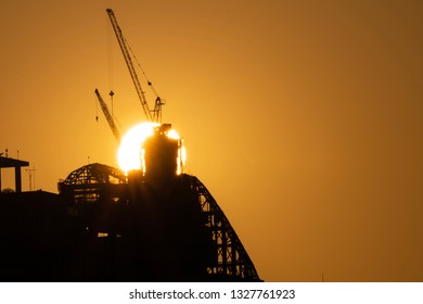 Silhouette of construction crane and developing city with the Sun setting behind the site 