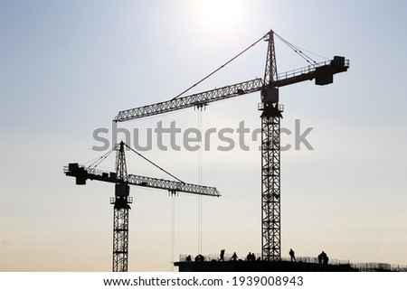 Silhouette of construction crane and workers on unfinished residential building against sunshine. Housing construction, apartment block in city