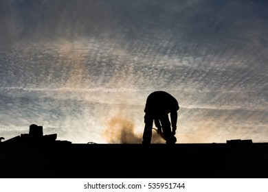 Silhouette of a construction worker cutting tile on a rooftop with an electric grinder, with the sunrise in the background - Powered by Shutterstock