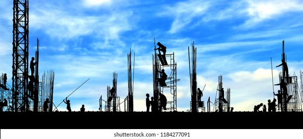 Silhouette Construction Workers Group Are Working To Build Reinforcement Structure On Top Of Building In Construction Site With Blurred Clouds And Blue Sky Background, Panorama View 