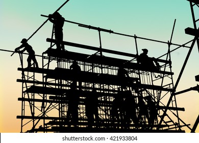 Silhouette Of Construction Workers Working On Scaffolding At A High Level By The Standards Set Must Include A Safety Belt For Safety. Heavy Industry And Safety At Work Concept.