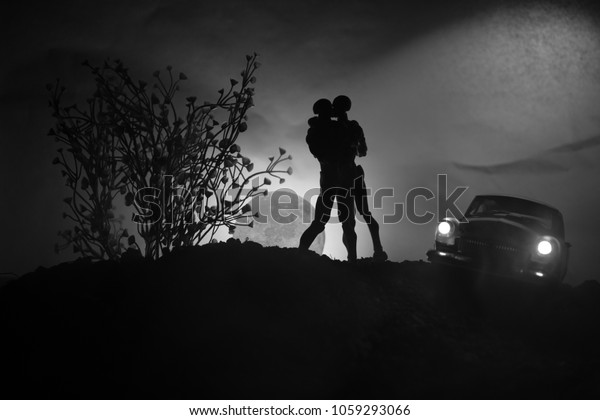 Silhouette of couple kissing under full moon. Guy\
kiss girl hand on full moon silhouette background. Valentine`s day\
decor concept. Car on back\
side
