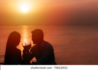 Silhouette of couple in love drinking wine during romantic dinner at sunset on the beach