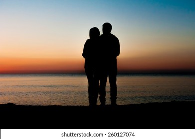 Silhouette of couple  on the beach looking at sunrise.