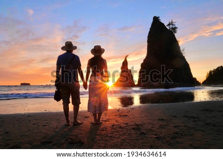 Silhouette of couple on beach walking towards rising sun with sea stacks on background. Rialto Beach. Washington. USA