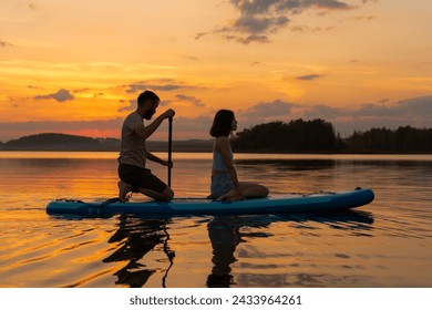 silhouette of couple paddleboarding at lake during sunset together. Concept of active family tourism and supping. Family enjoy vacation - Powered by Shutterstock