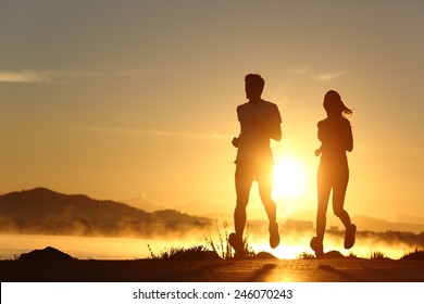 Silhouette Of A Couple Running At Sunset With The Sun In The Background